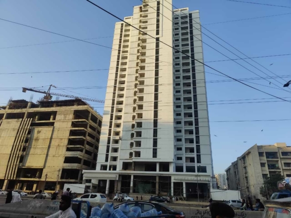 Tall white high-rise apartment tower under construction with cranes and urban street scene.